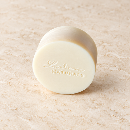 Angled view of one round ivory Aloe Quench conditioner bar with the Lustera Naturals stamp on warm ivory stone