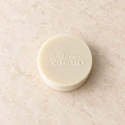 Top view of an ivory Aloe Quench conditioner bar lying flat with the Lustera Naturals stamp