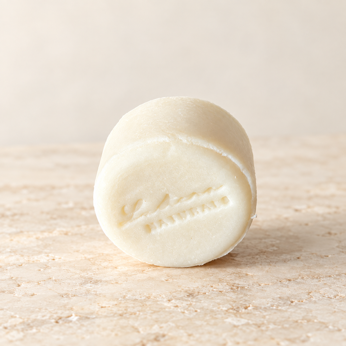 Angled view of one ivory Aloe Quench shampoo bar with the Lustera Naturals stamp and softly lit ivory background