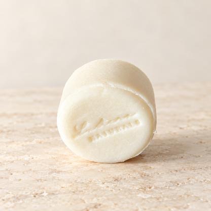 Angled view of one ivory Aloe Quench shampoo bar with the Lustera Naturals stamp and softly lit ivory background