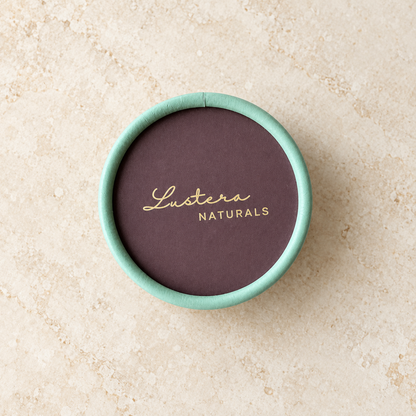 Top view of the mint-green and plum Lustera Naturals shampoo bar box on warm ivory stone