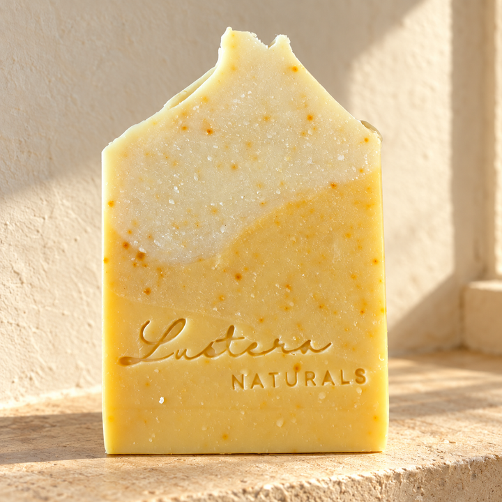 Golden Sunrise handmade soap bar with cream and golden layers and annatto speckles on a sunlit ledge