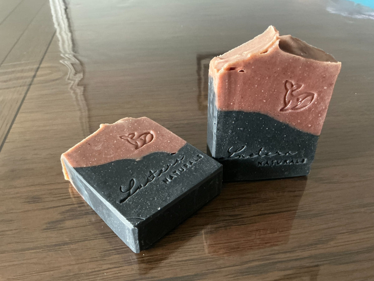 Close view of one standing and one flat Meliya Aanmai soap bar showing natural speckles, two-tone layers and stamped designs