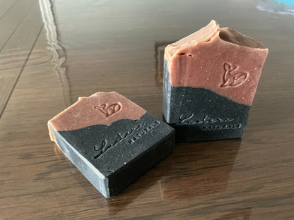 Close view of one standing and one flat Meliya Aanmai soap bar showing natural speckles, two-tone layers and stamped designs