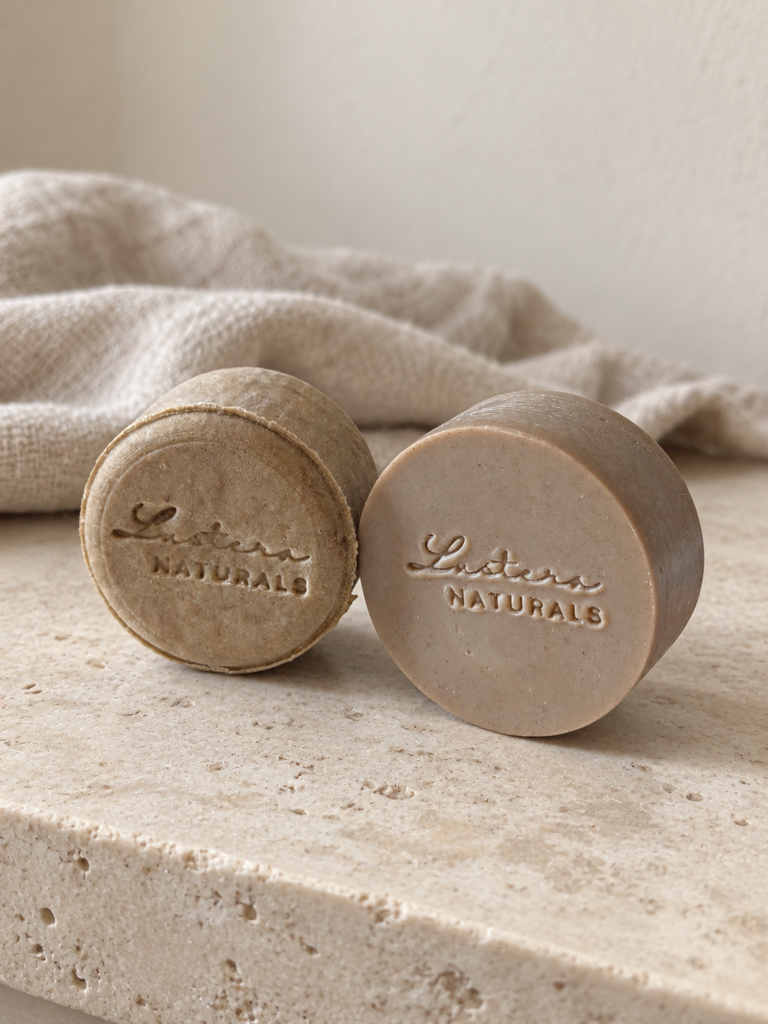 Scalp Sanctuary shampoo and conditioner bars on pale limestone with loosely folded linen